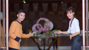 A man and a woman standing in a lobby with a table of flowers in the background. - Muong Thanh Luxury Buon Ma Thuot (Tan An)