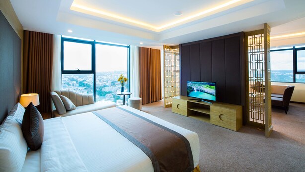 A hotel room with a large bed, a TV, a desk, and a view of the city. - Muong Thanh Luxury Buon Ma Thuot (Tan An)
