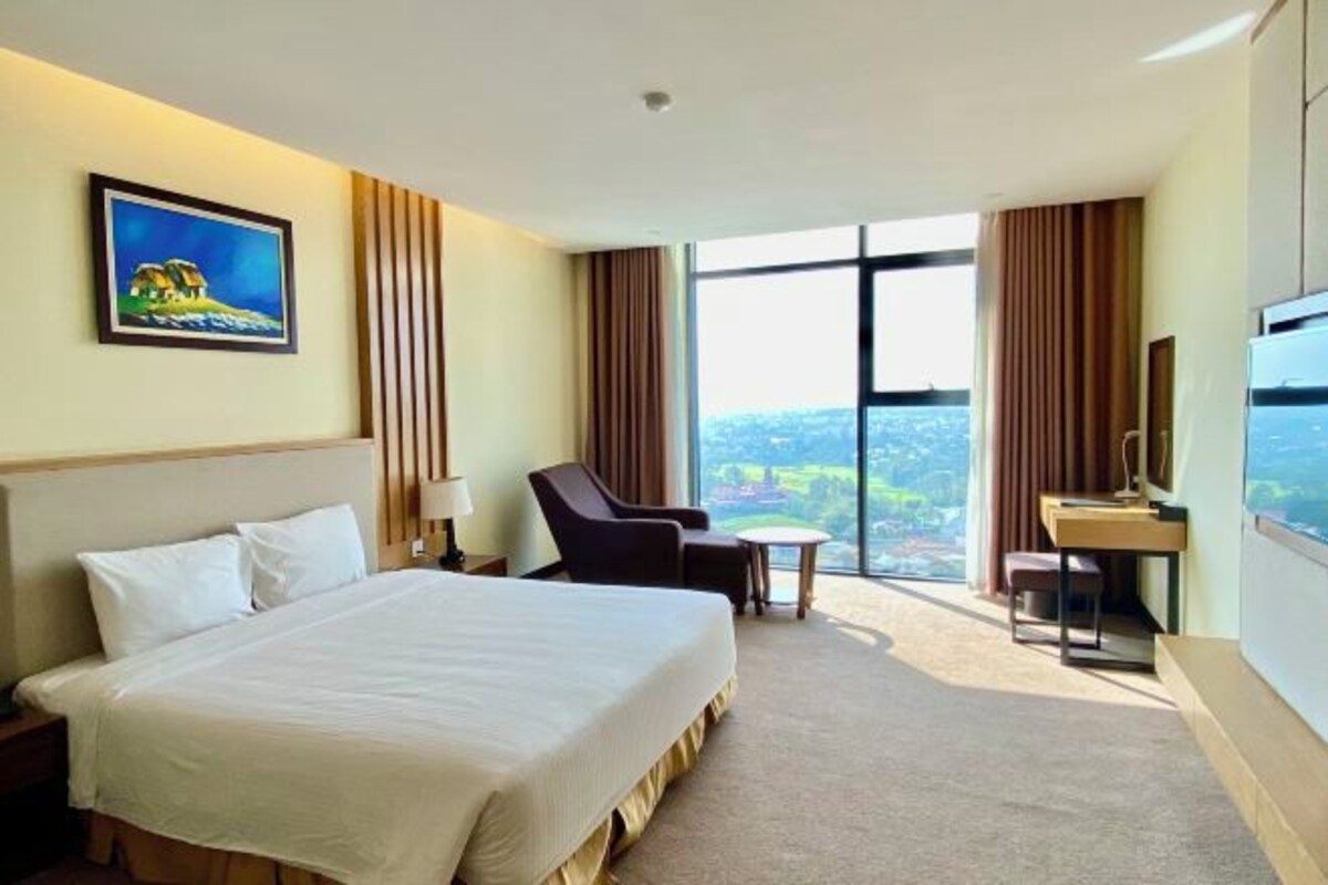 Habitación de hotel con una cama grande, un escritorio, una silla y un televisor. Hay una ventana con vistas a la ciudad.