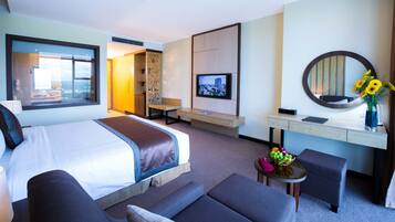 A hotel room with a large bed, a desk with a computer, a TV, a mirror, and a vase with flowers.