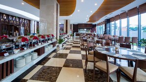 A buffet area with multiple serving stations, a checkered floor, and a view of the kitchen in the background. - Muong Thanh Luxury Buon Ma Thuot (Tan An)
