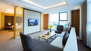 A modern hotel room with a sofa, a TV, a coffee table, and a view of the city. - Muong Thanh Luxury Buon Ma Thuot (Tan An)