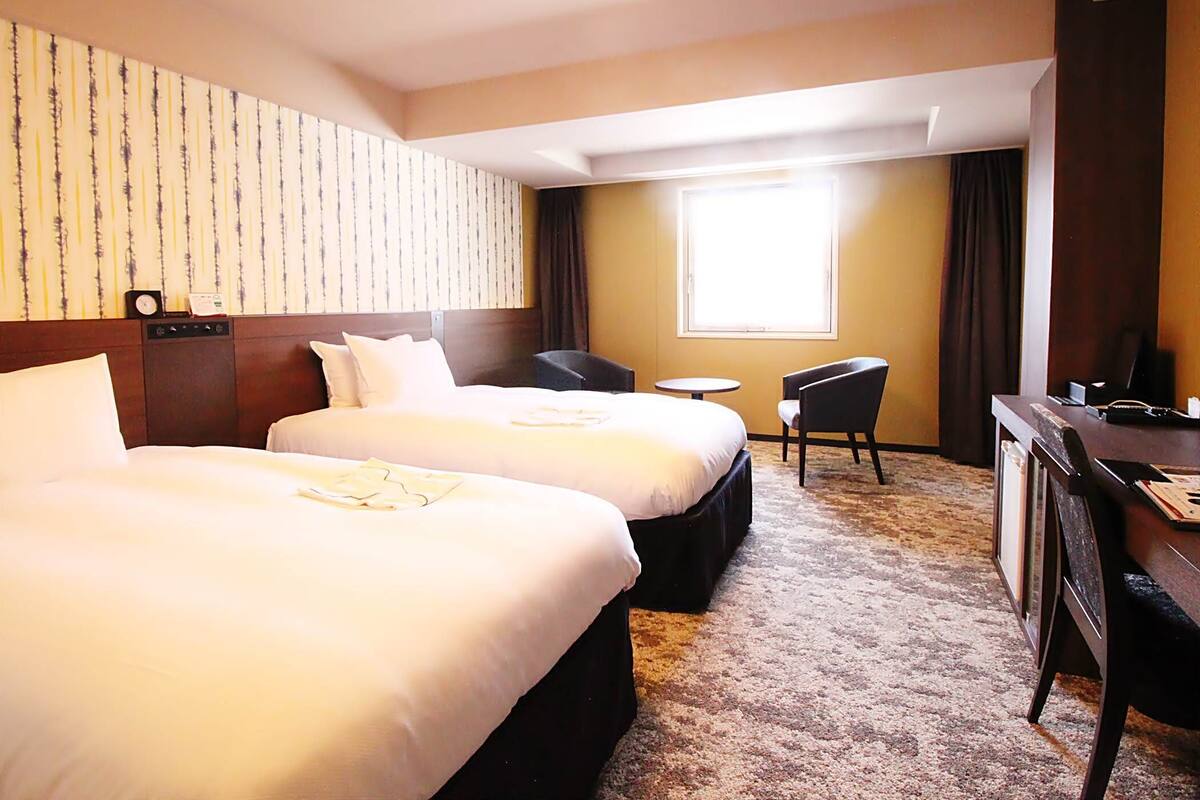 Ein Hotelzimmer mit zwei Betten, einem Schreibtisch, einem Stuhl und einem kleinen Tisch.