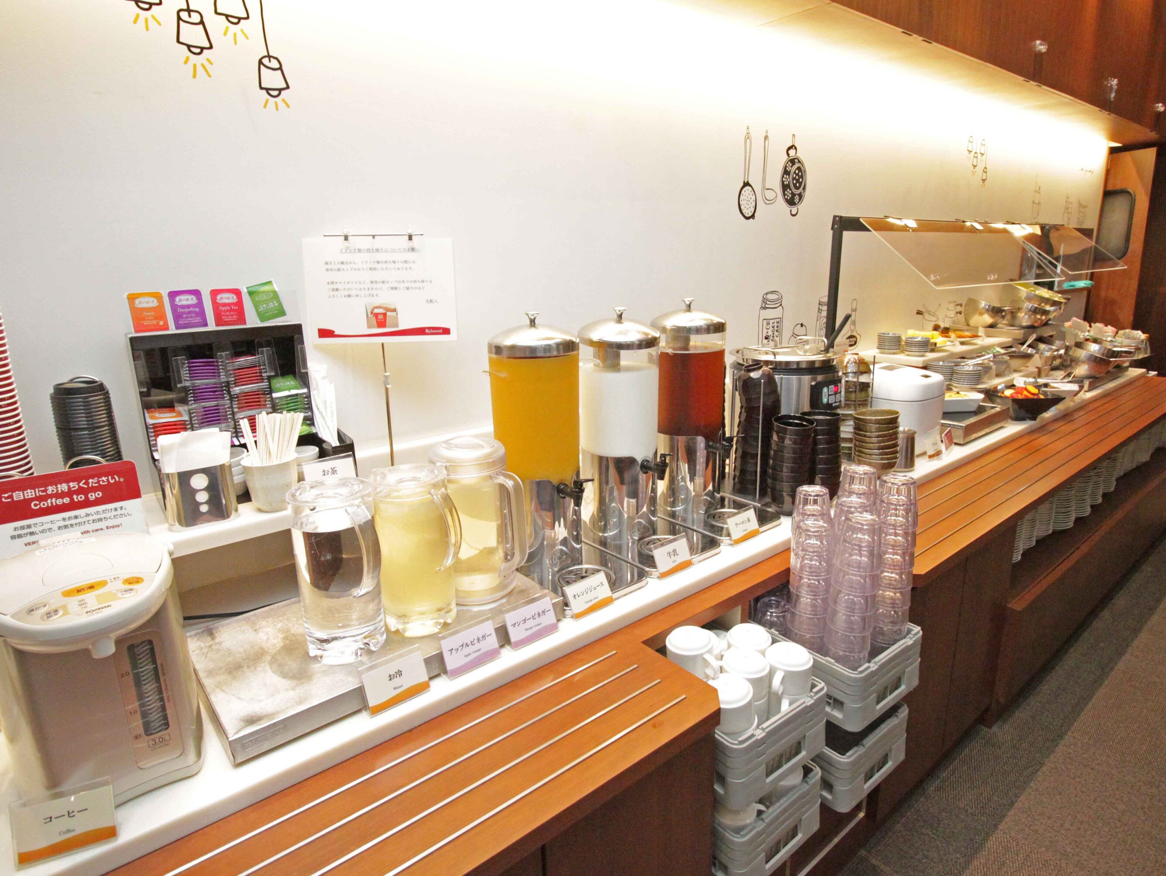 Un buffet proposant une variété de plats et de boissons, notamment des distributeurs de café et de thé, ainsi qu’un panneau indiquant que du café est disponible.