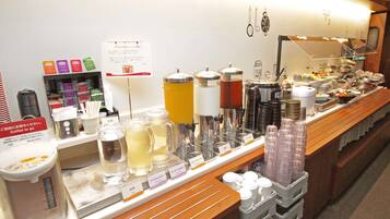 Un buffet proposant une variété de plats et de boissons, notamment des distributeurs de café et de thé, ainsi qu’un panneau indiquant que du café est disponible.