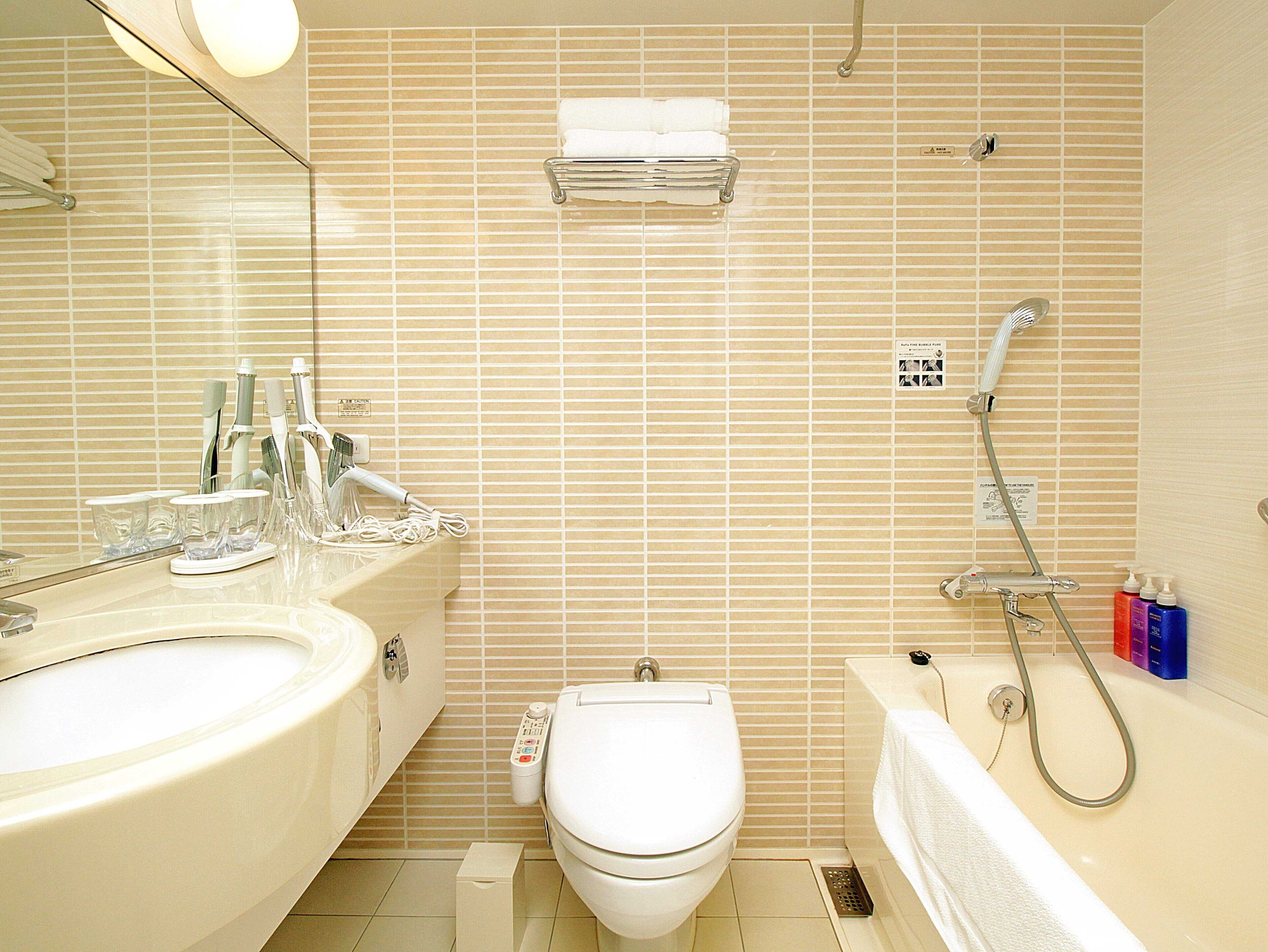 Un baño con lavamanos, inodoro y bañera, equipado con cabezal de ducha y dispensadores de jabón para manos.