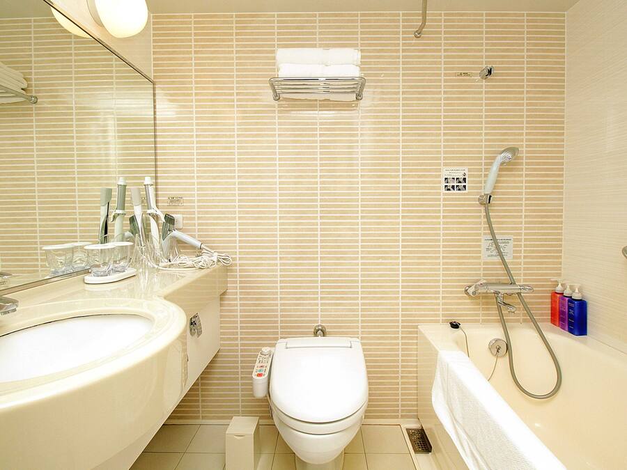 Un baño con lavamanos, inodoro y bañera, equipado con cabezal de ducha y dispensadores de jabón para manos.