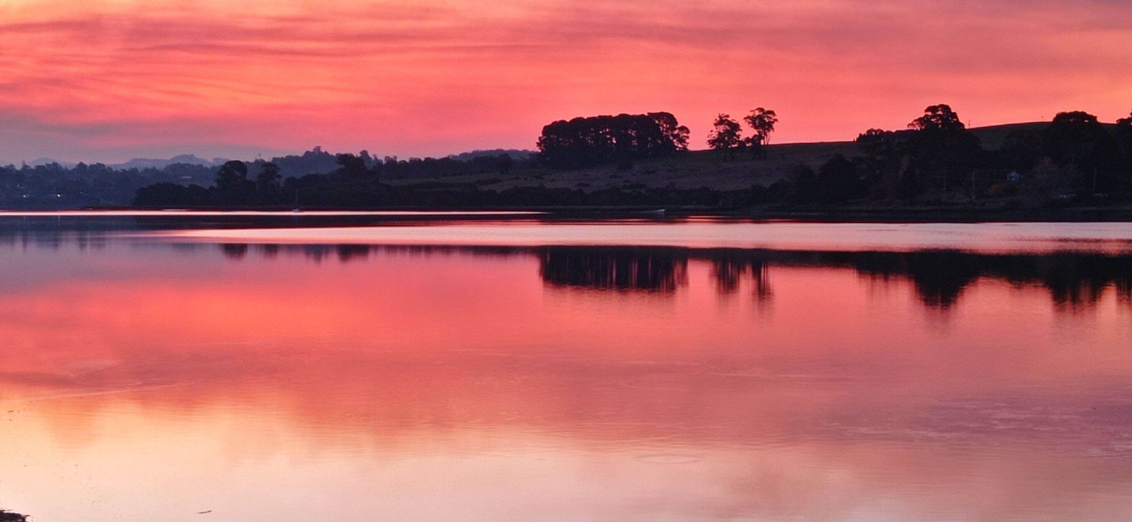 Un lago tranquilo al atardecer, con el reflejo del cielo y los árboles en la superficie del agua.