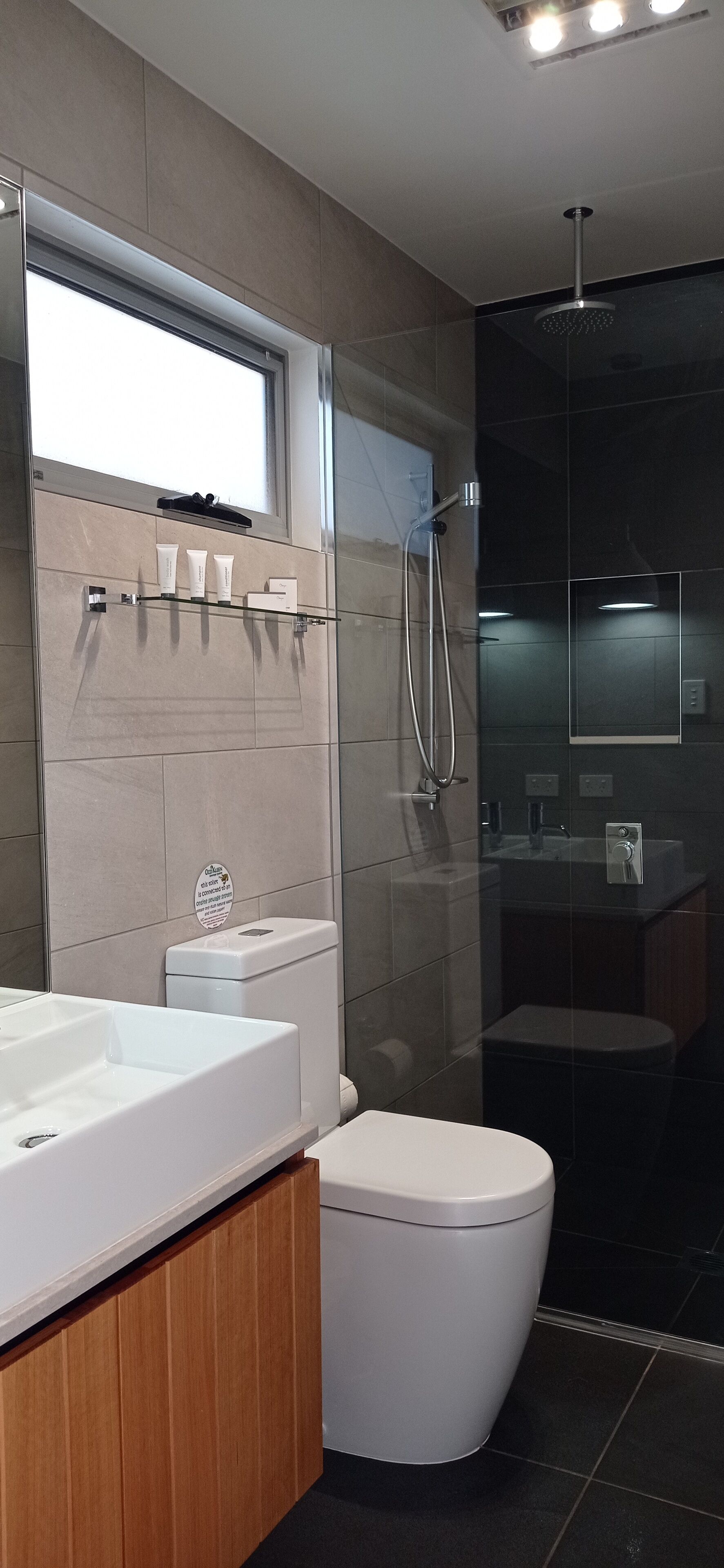 Une salle de bain moderne avec une douche à parois de verre, des toilettes blanches et un meuble-lavabo avec un miroir.