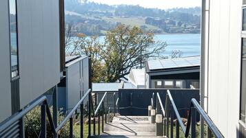A view from a window overlooking a body of water, a tree, and a building with a staircase leading to a deck.