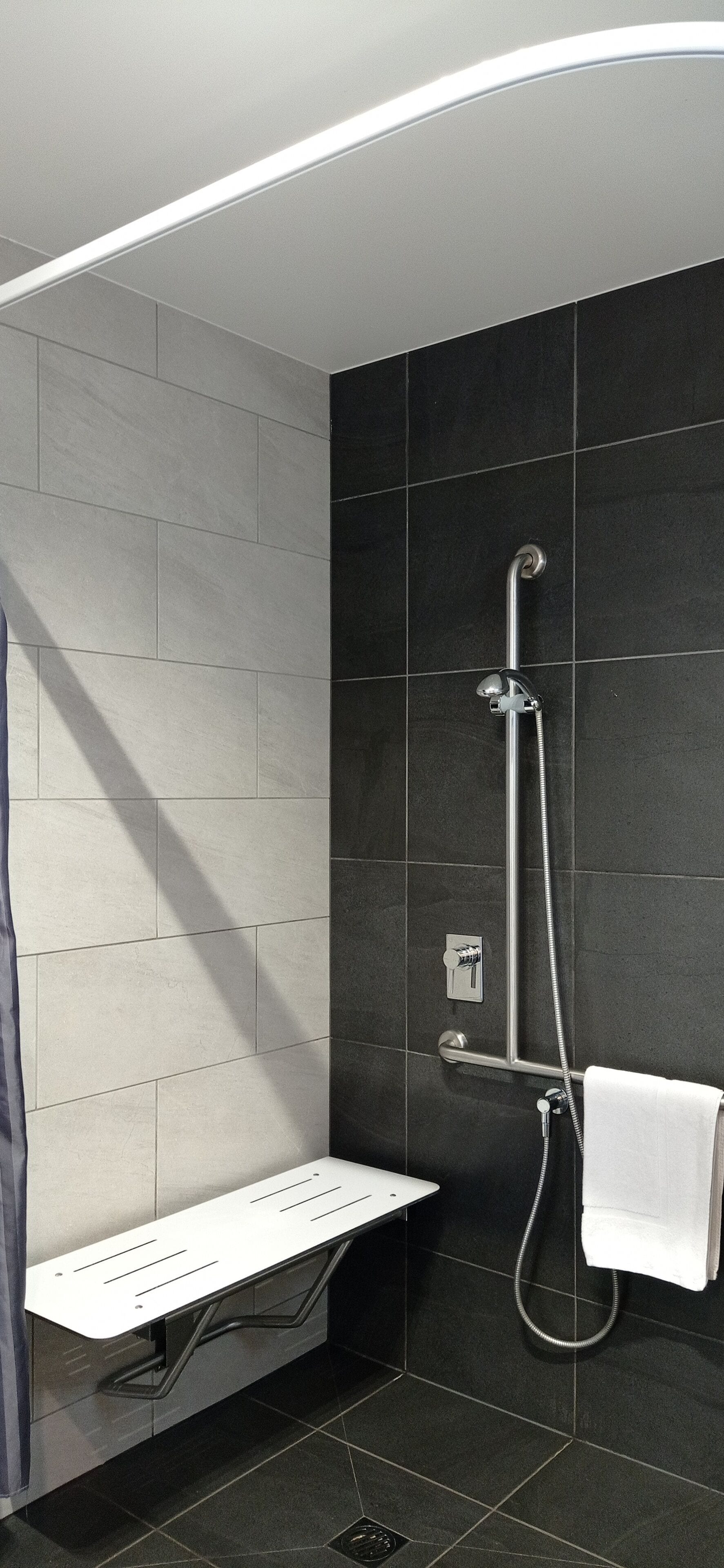 Un baño moderno con ducha de mano, asiento integrado y perchero para toallas.