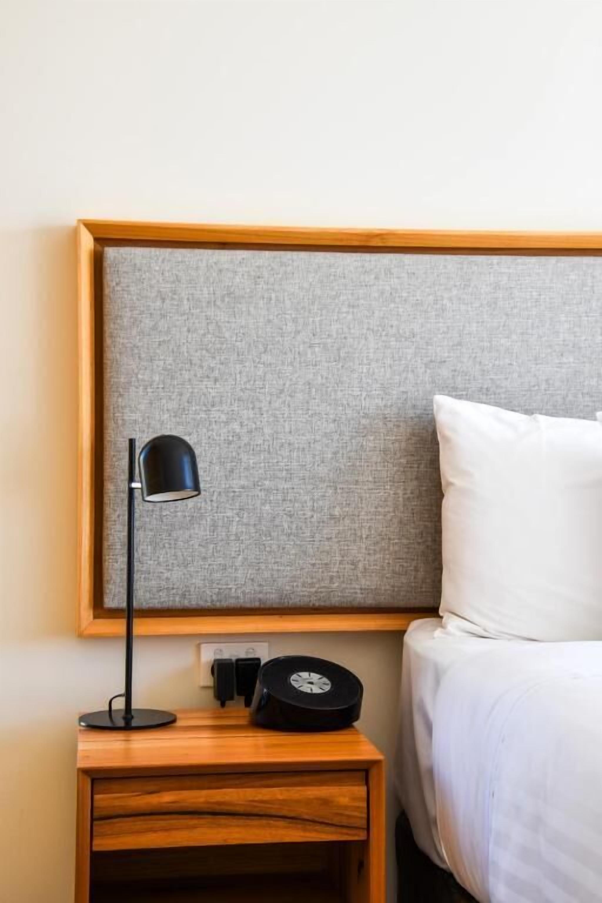 A neatly made bed with a white pillow and a grey headboard.