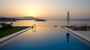An infinity pool with a clear view of the sunset over the water, lounge chairs, and an umbrella. - Sk Place Crete Luxury Seafront Villas (Apokoronas)