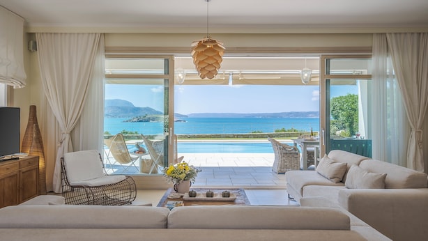 A modern living room with a sofa, a chair, a table with a vase, and a view of the sea. - Sk Place Crete Luxury Seafront Villas (Apokoronas)