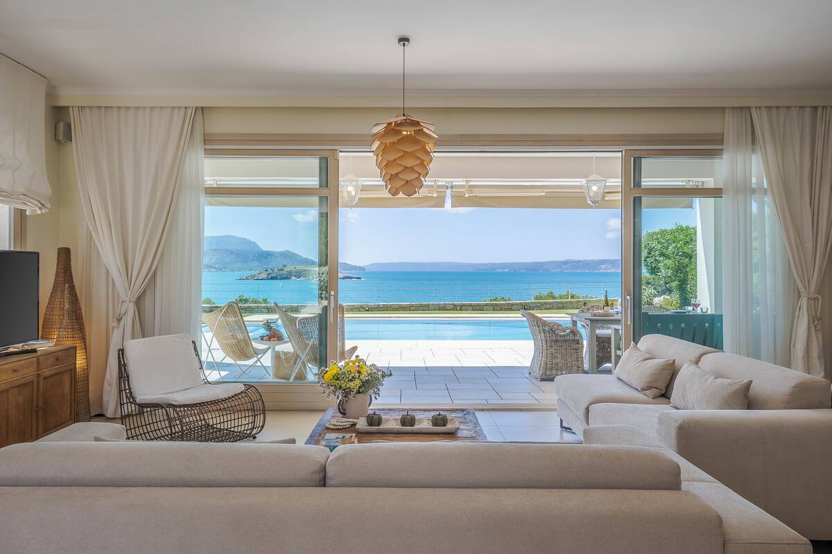 A modern living room with a sofa, a chair, a table with a vase, and a view of the sea.