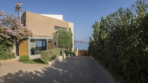 A modern building with a paved driveway, a glass entrance, and a view of the sea. - Sk Place Crete Luxury Seafront Villas (Apokoronas)