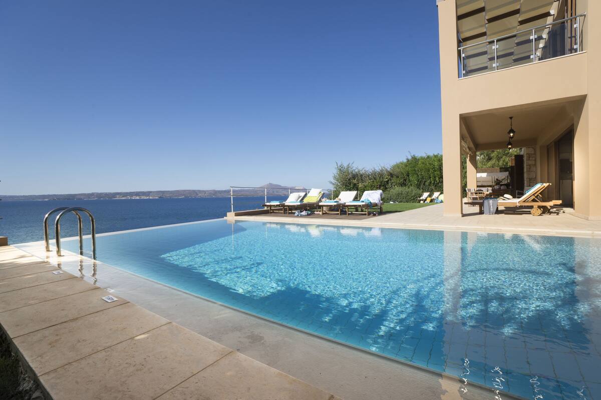 A pool area with lounge chairs and a view of the sea.