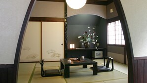 A traditional Japanese room with tatami flooring, a low table with a tea set, a chair, and a vase with flowers.