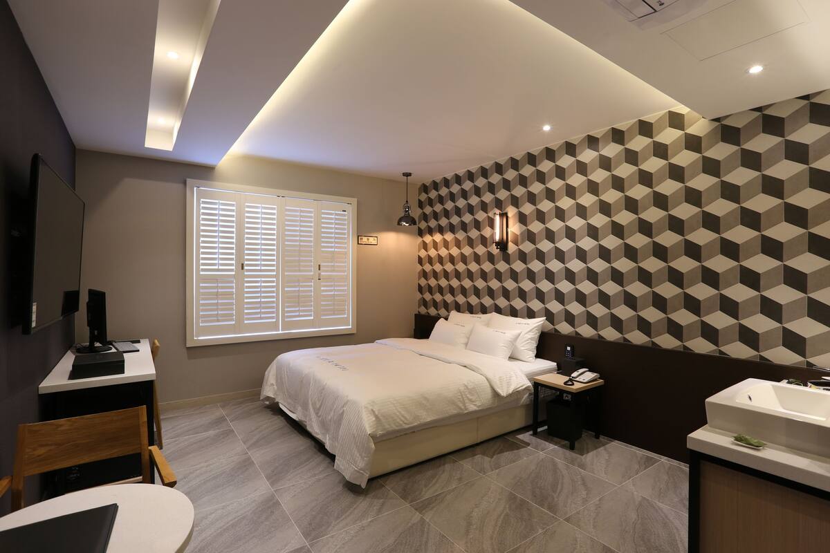 Un dormitorio moderno con cama, mesita de noche y baño con lavabo y espejo.