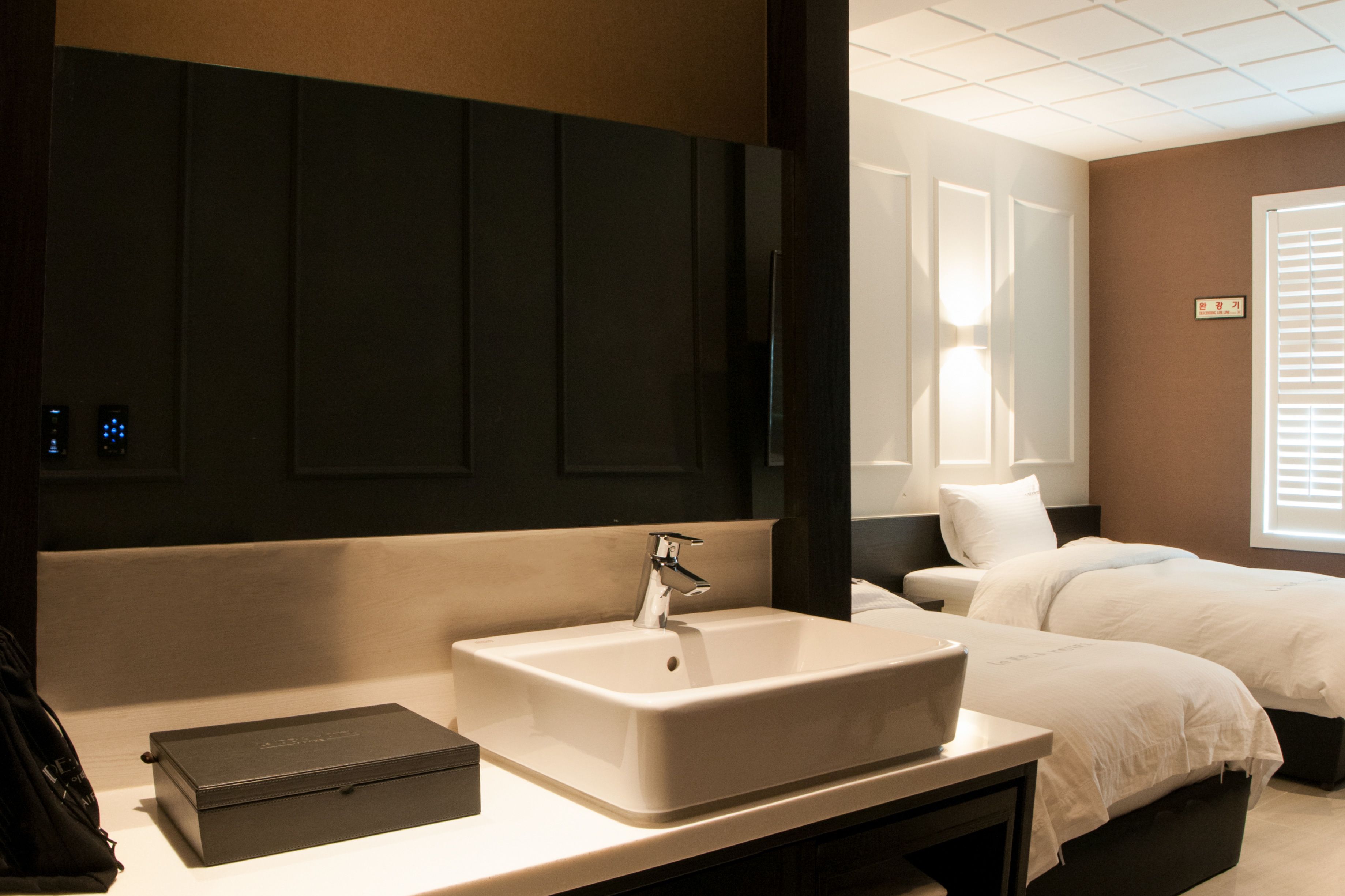 A hotel room with a large white sink, a bedside table, a black suitcase, and a bed with white bedding.
