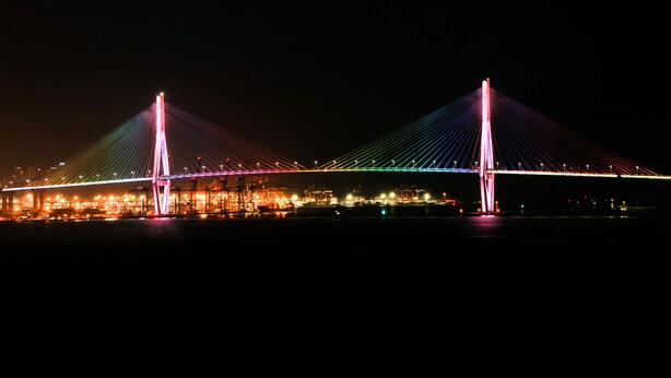 Une vue nocturne d'un pont dont les câbles et les pylônes sont illuminés.