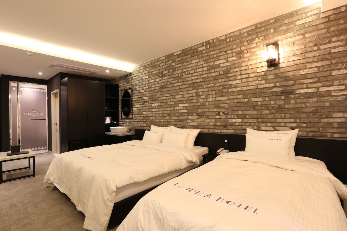 Una habitación de hotel con dos camas, una pared de ladrillo, una mesita de noche y un armario.