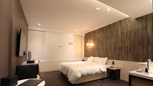 Une chambre d’hôtel moderne équipée d’un lit, d’une table de chevet, d’un bureau, d’une chaise et d’un téléviseur fixé au mur.