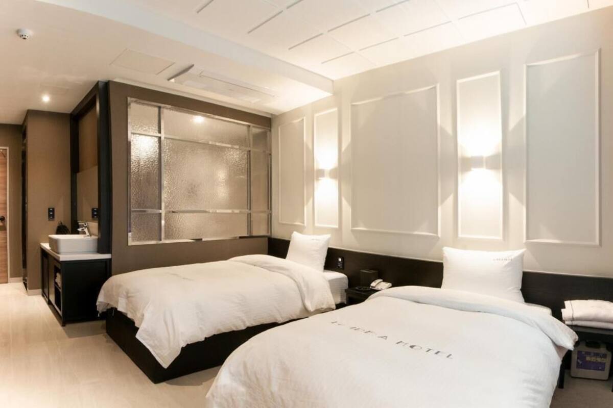 Habitación de hotel con dos camas, un espejo grande, una mesita de noche con un teléfono y un mueble pequeño con un lavabo.