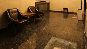 Un hall d’entrée avec un comptoir de réception, deux fauteuils, une petite table et un sol en blocs de verre.