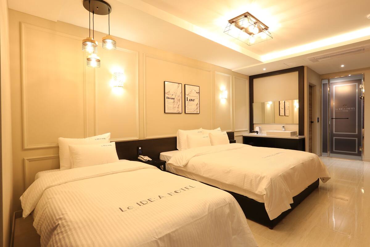 Habitación de hotel con dos camas, un espejo grande, una mesita de noche y un baño con lavamanos y espejo.