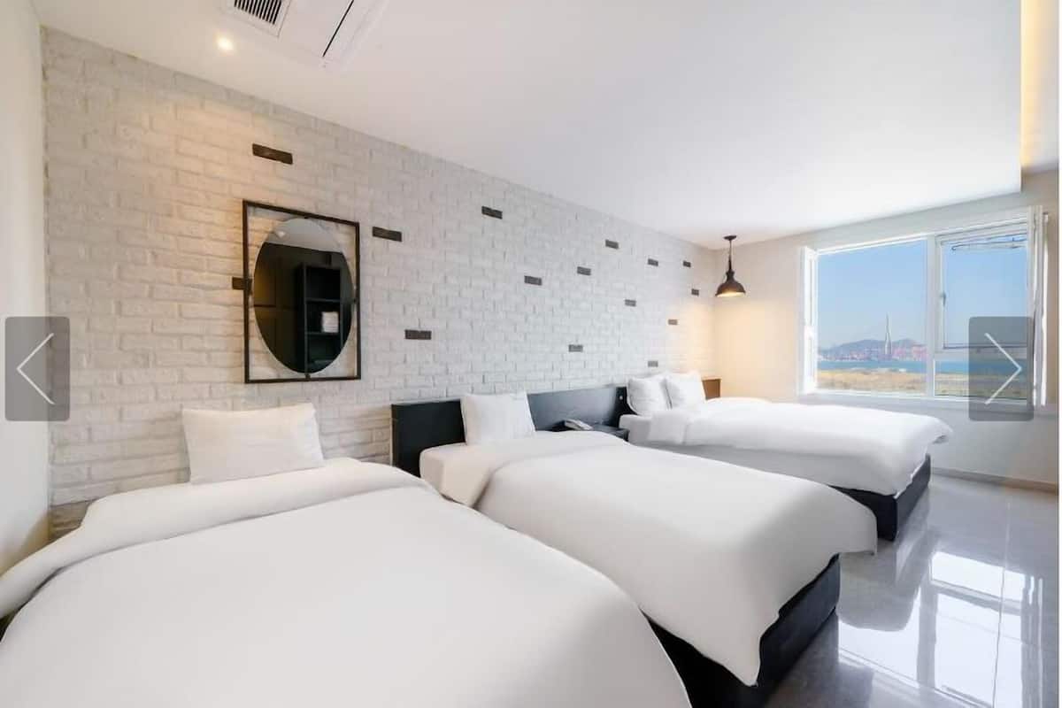 Una habitación de hotel moderna con tres camas, un ventanal con vistas a la ciudad y una pared de ladrillo con un espejo.