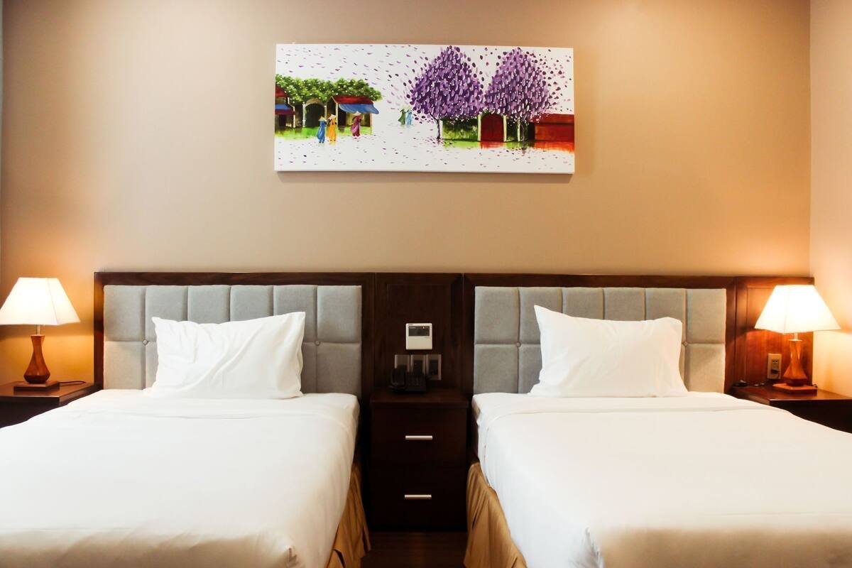 A hotel room with two beds, a nightstand, a lamp, and a painting on the wall.