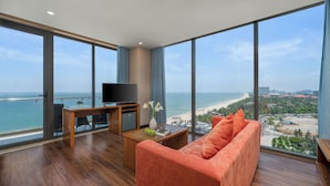 A modern room with a large window, a flat-screen TV, a wooden coffee table, a sofa, and a small desk. - Yarra Ocean Suites Danang (Da Nang)