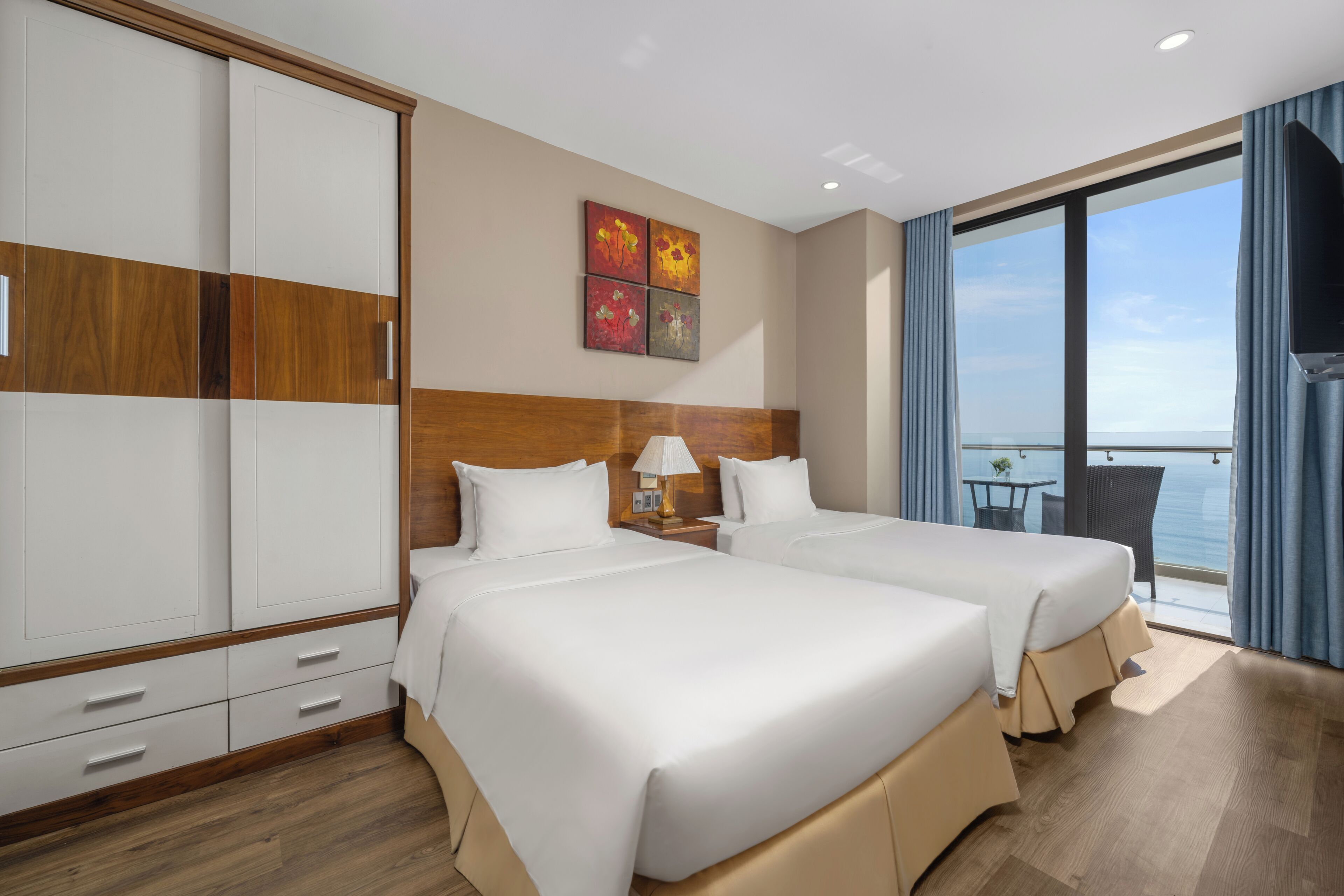 Une chambre d’hôtel avec deux lits, une armoire, des œuvres d’art au mur et un balcon avec vue.