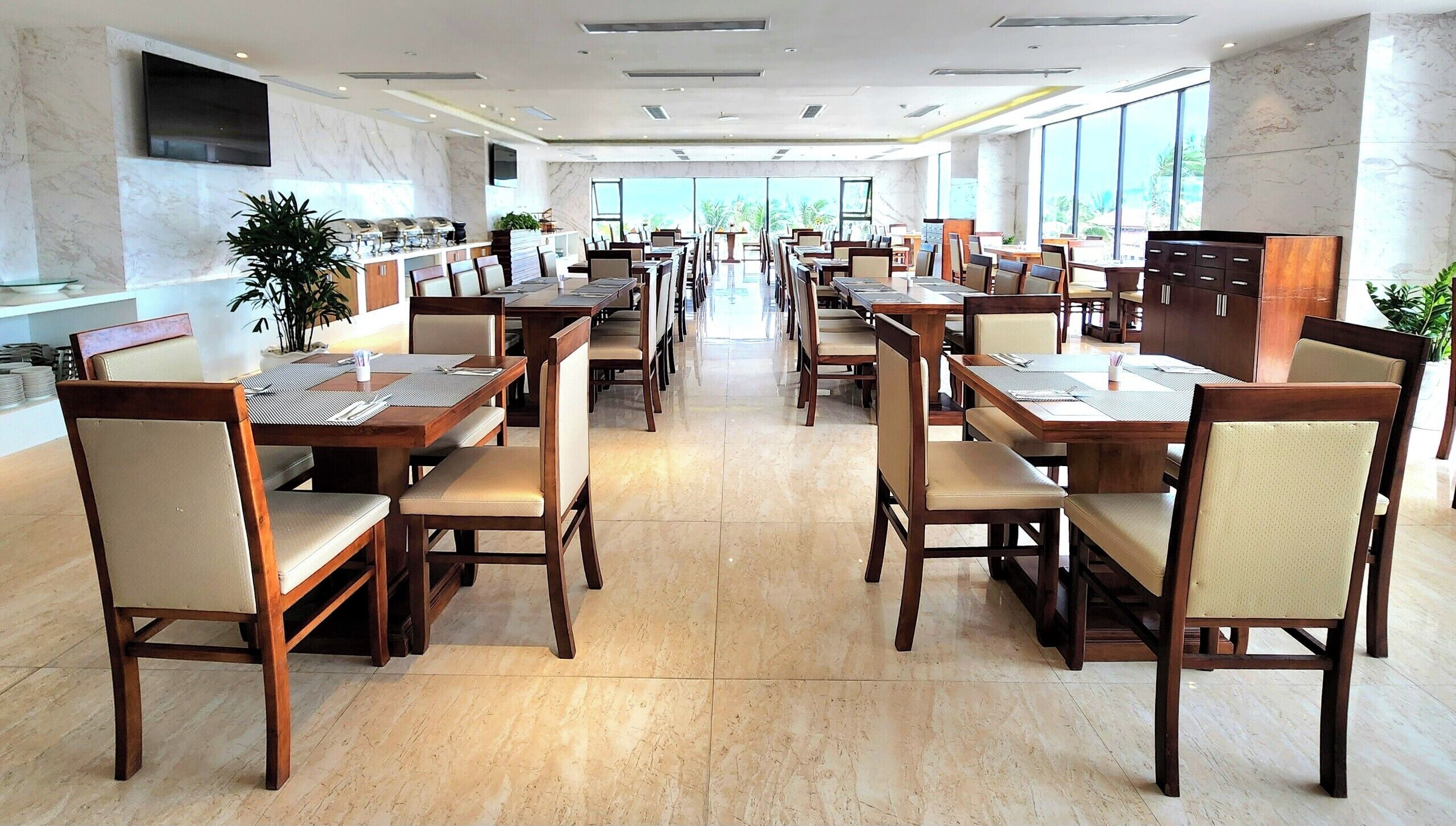 Uma ampla área de refeições com várias mesas e cadeiras, um buffet e grandes janelas com vista.