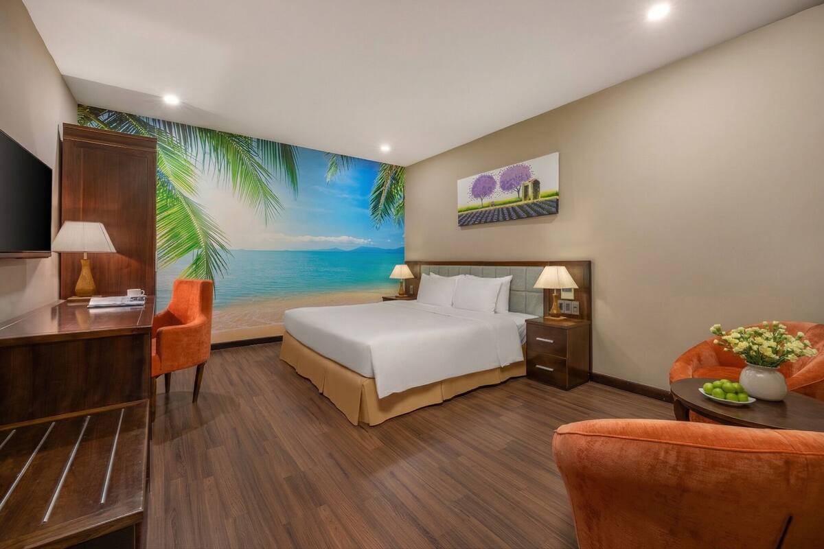 A hotel room with a bed, desk, chair, and a mural of a beach scene.
