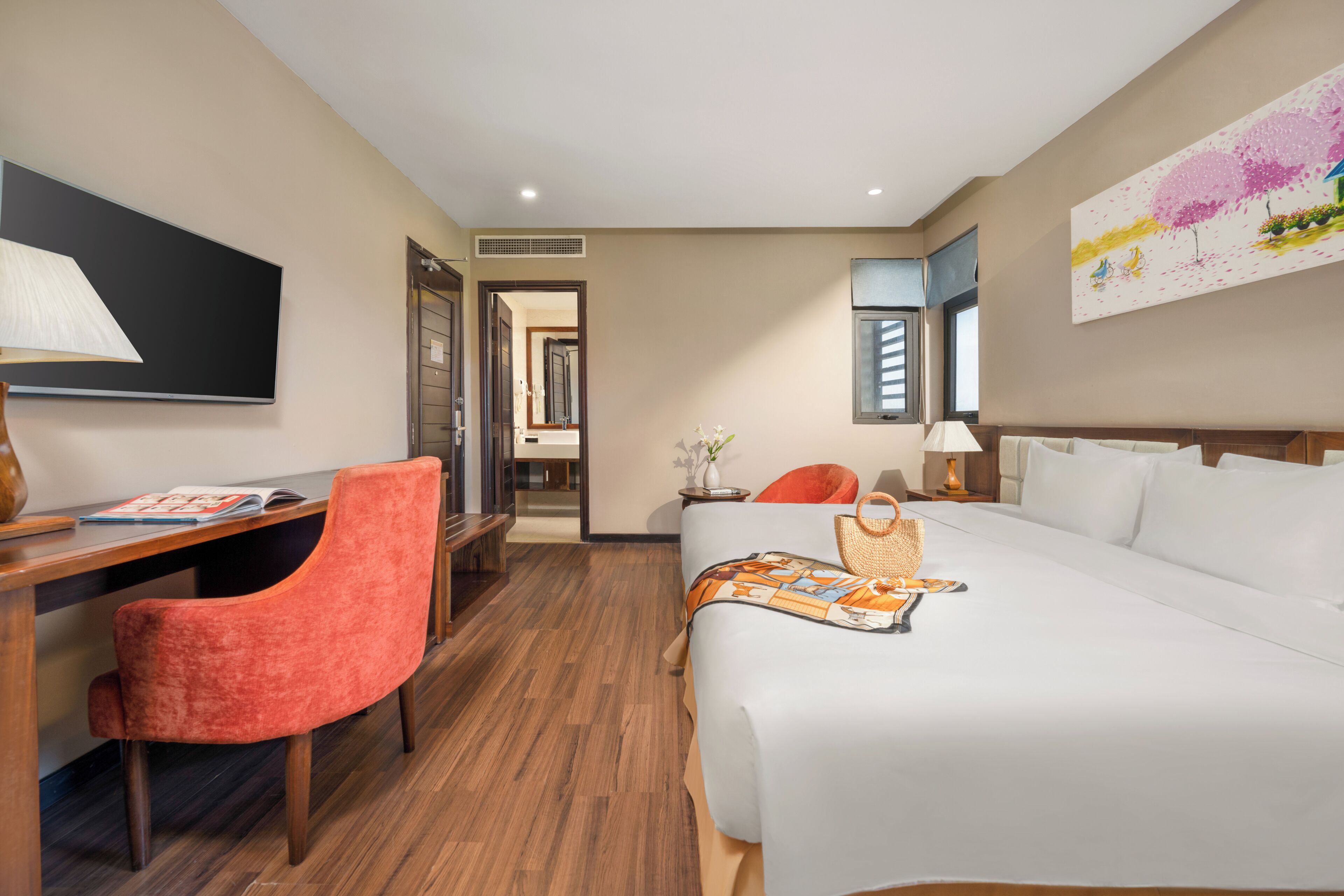 A hotel room with a bed, a desk, a chair, a TV, and a painting on the wall.