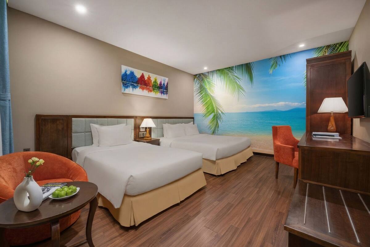 A hotel room with two beds, a desk, a chair, a TV, and a mural of a beach scene.