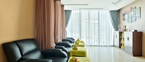 Une chambre d’hôtel avec une rangée de fauteuils de massage, un comptoir d’accueil et une grande fenêtre avec des rideaux.