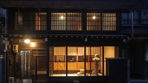 Il s'agit d'un bâtiment traditionnel japonais, avec une façade en bois, une entrée bien visible et une lanterne en pierre placée au premier plan.