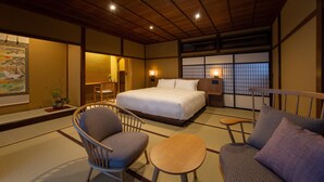 Une pièce de style japonais traditionnel, avec un sol recouvert de tatamis, un grand lit, un canapé, une petite table et une porte coulissante donnant sur un paysage.