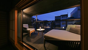 Un balcon aménagé avec un lit, une chaise et une table, offrant une vue sur le paysage urbain au crépuscule.