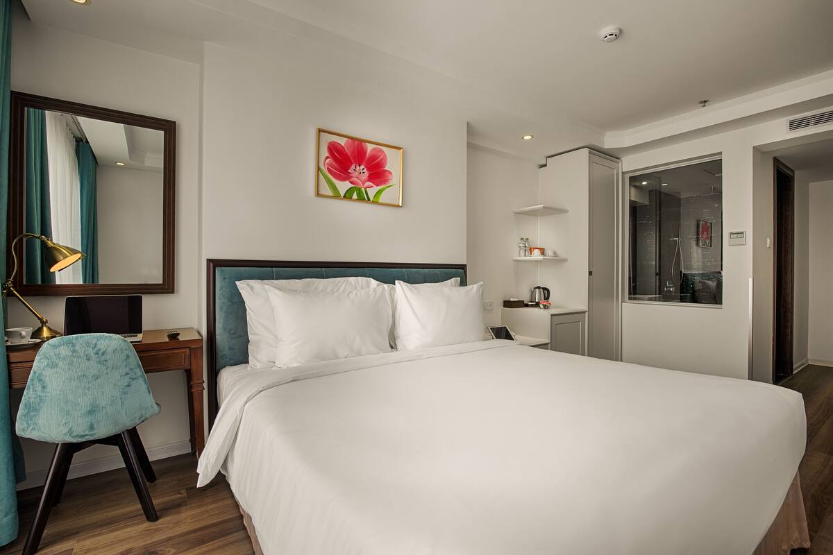 Une chambre d’hôtel avec un grand lit, un bureau avec un ordinateur portable, une chaise, un miroir et un tableau au mur.