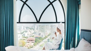 A hotel room with a large arched window, a bed with white linens, and teal curtains. - Adaline Hotel & Suite (Da Nang)