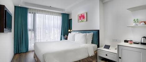 Une chambre d’hôtel avec un grand lit, un bureau avec un ordinateur portable, une armoire à chaussures et une fenêtre avec des rideaux.