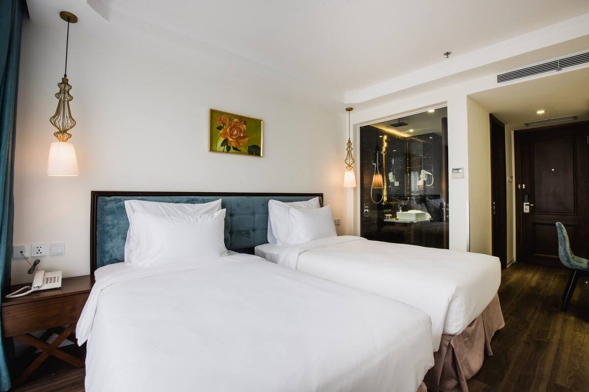 Une chambre d’hôtel avec deux lits, un tableau représentant une rose, un téléphone et un miroir.