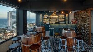 A bar with wooden barrels and stools, a view of the city, and a bar counter with bottles. - Adaline Hotel & Suite (Da Nang)
