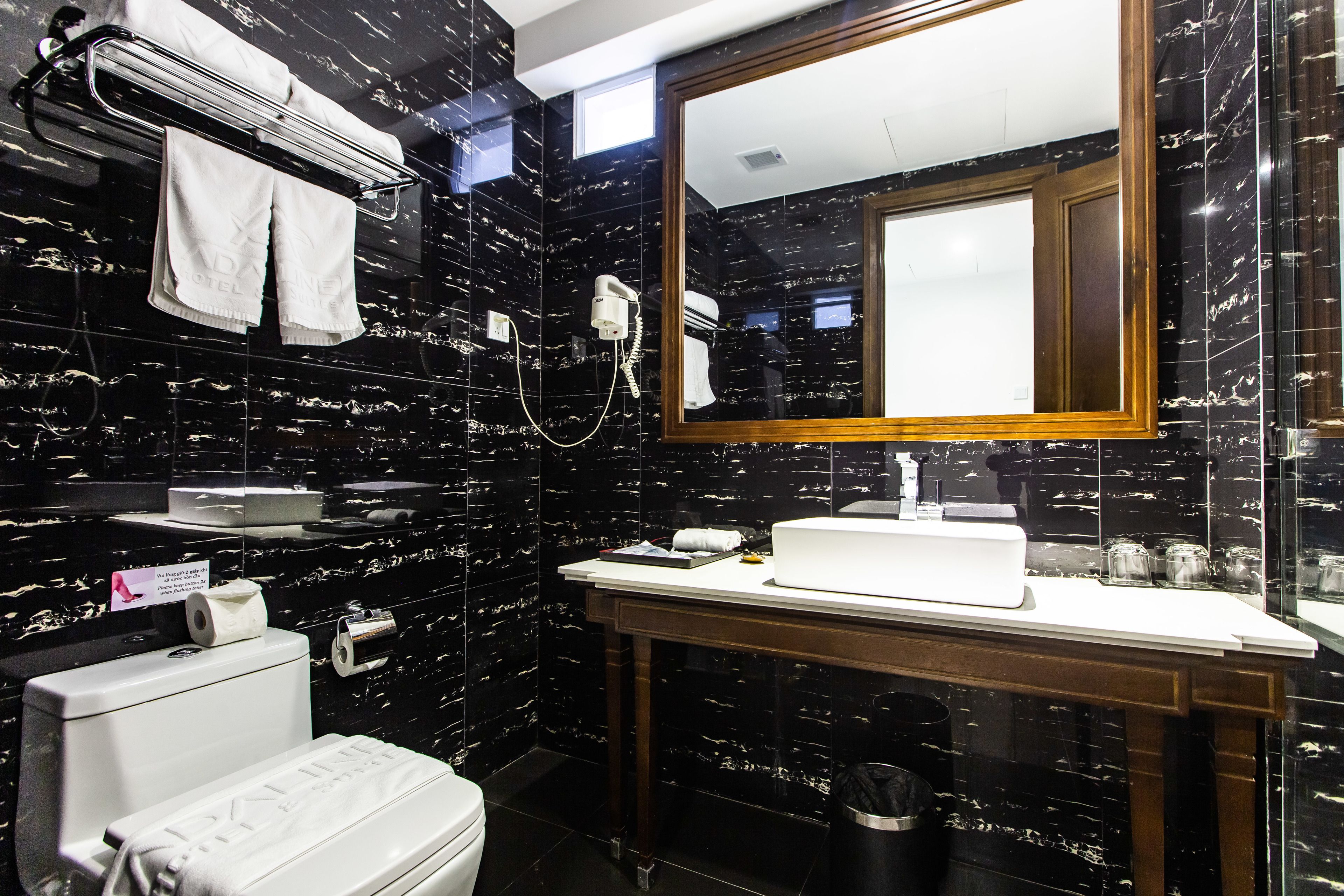 A bathroom with a black marble wall, a white sink, a mirror, a towel rack, and a toilet.