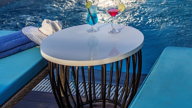 A poolside area with a table and two drinks, overlooking a body of water and mountains. - Adaline Hotel & Suite (Da Nang)