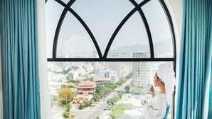 A person sitting by a window with a view of a cityscape, curtains, and a chair. - Adaline Hotel & Suite (Da Nang)